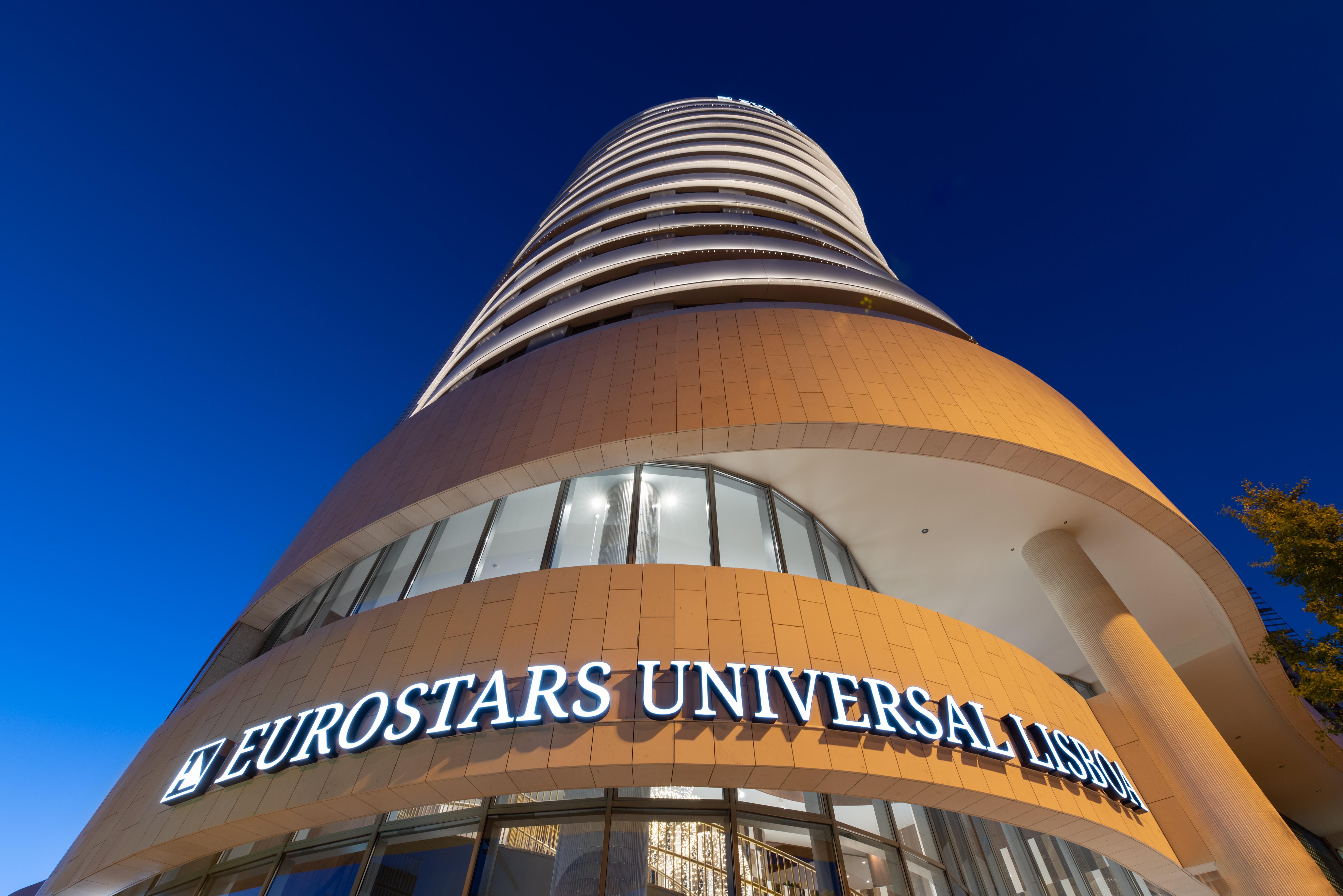 Отель Eurostars Universal Lisboa Экстерьер фото The photo shows a modern hotel building known as Eurostars Universal Lisbon. The structure is tall and features a curved design, with multiple floors and large windows. The hotel's name is prominently displayed in illuminated letters at the bottom, a