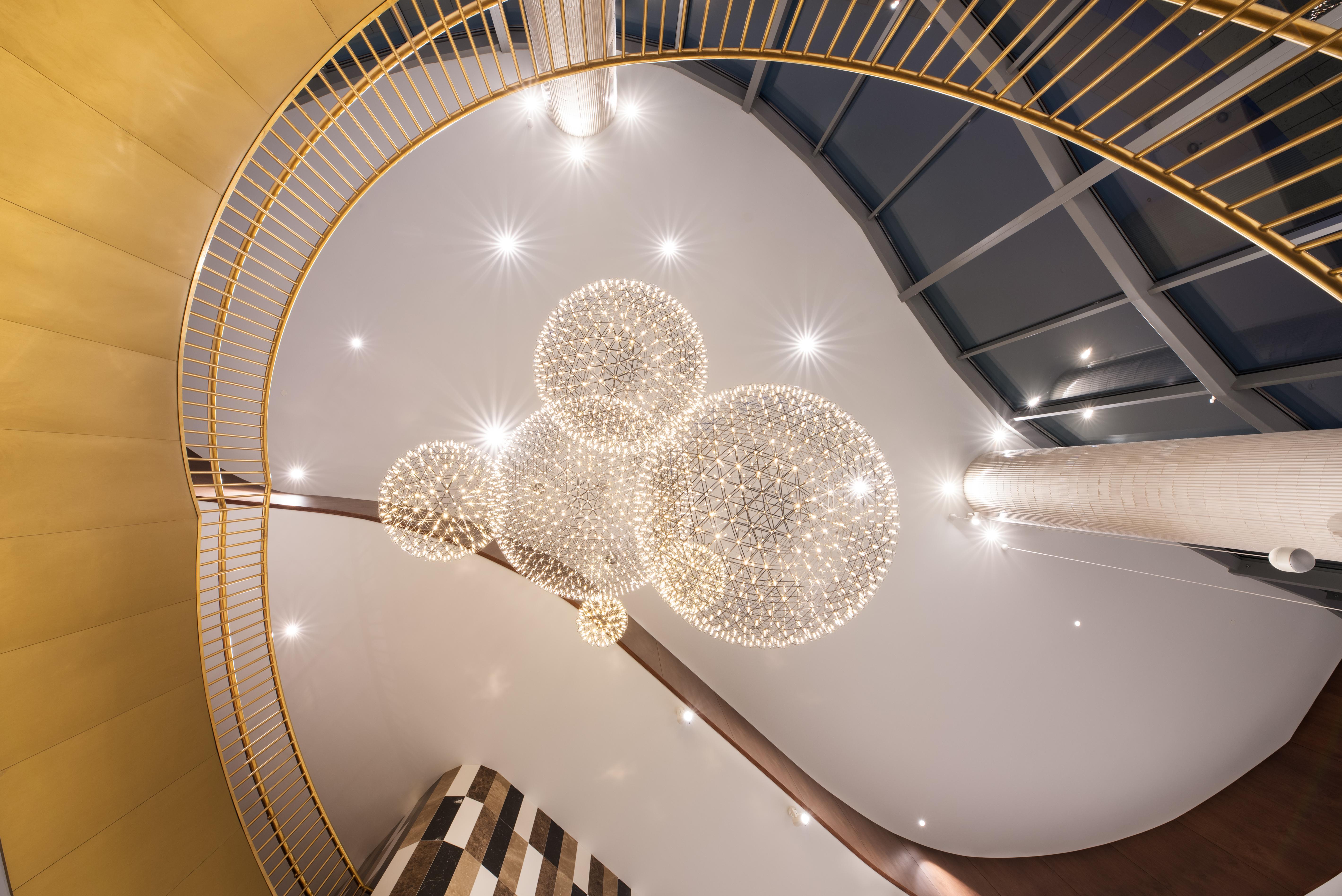 Отель Eurostars Universal Lisboa Экстерьер фото The photo shows an interior space viewed from below, showcasing a spiraling staircase with a golden railing. Above, there are several elegant spherical chandeliers that emit soft, ambient light. The ceiling is smooth and features recessed lighting, c