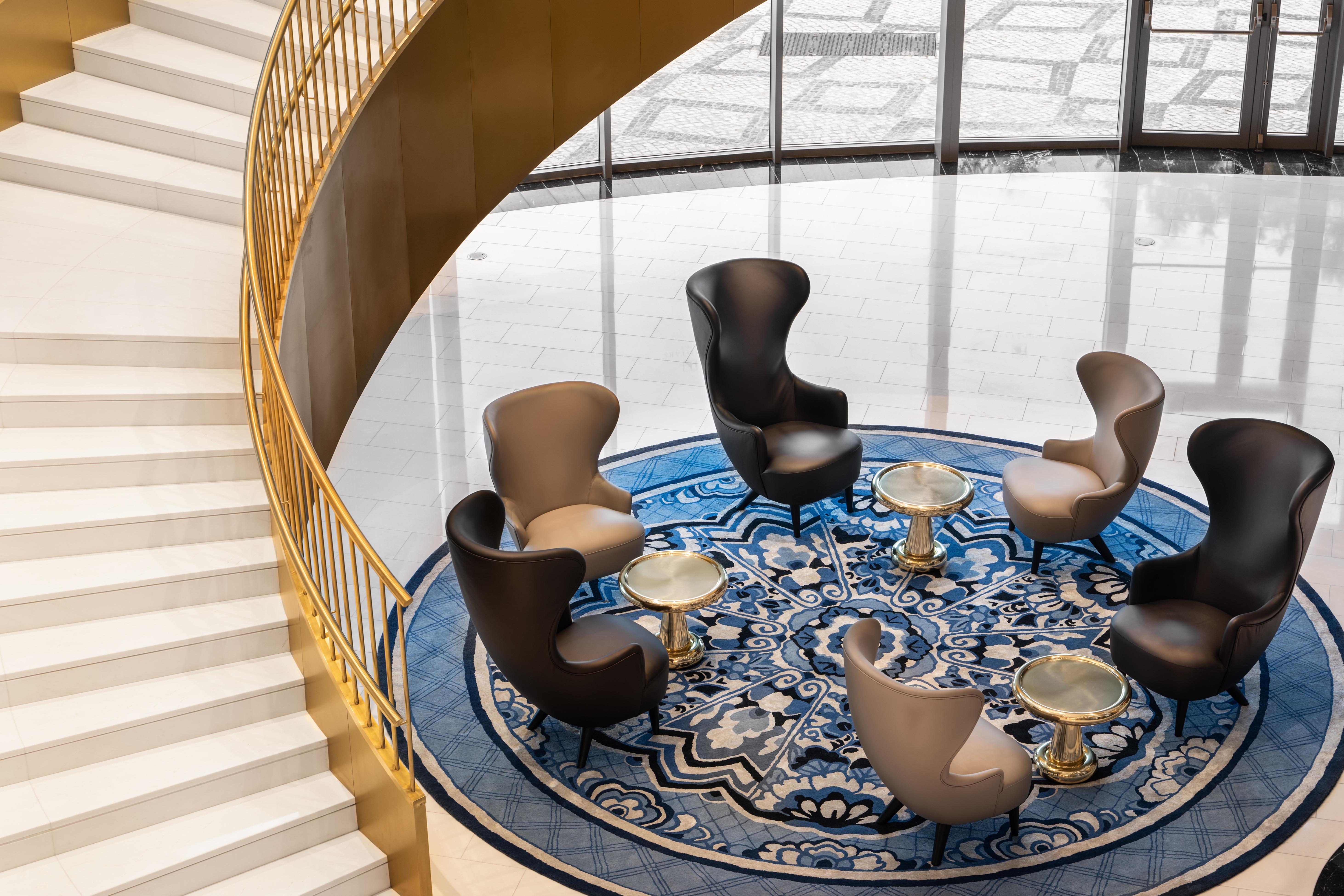 Отель Eurostars Universal Lisboa Экстерьер фото The photo shows a stylish lounge area featuring an elegant, modern design. In the center, there is a round blue rug with intricate patterns. Surrounding the rug are several contemporary chairs in various colors—two in light beige and two in black. Sm