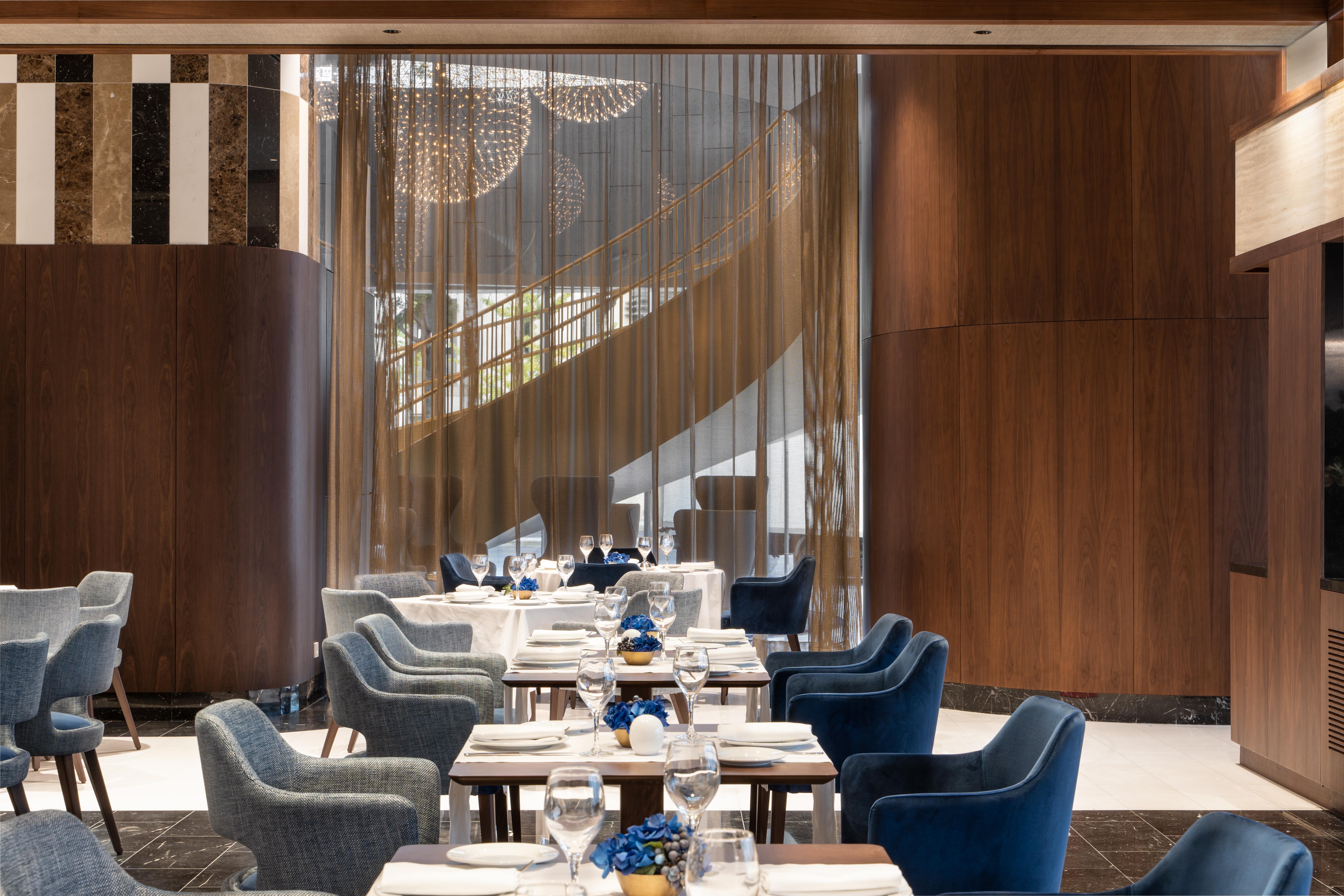 Отель Eurostars Universal Lisboa Экстерьер фото The photo depicts a stylish dining area in a modern restaurant. The decor features a warm wood paneling contrast with sleek furnishings. There are several tables arranged in the space, each set with white tablecloths and elegant blue decorations. Sof