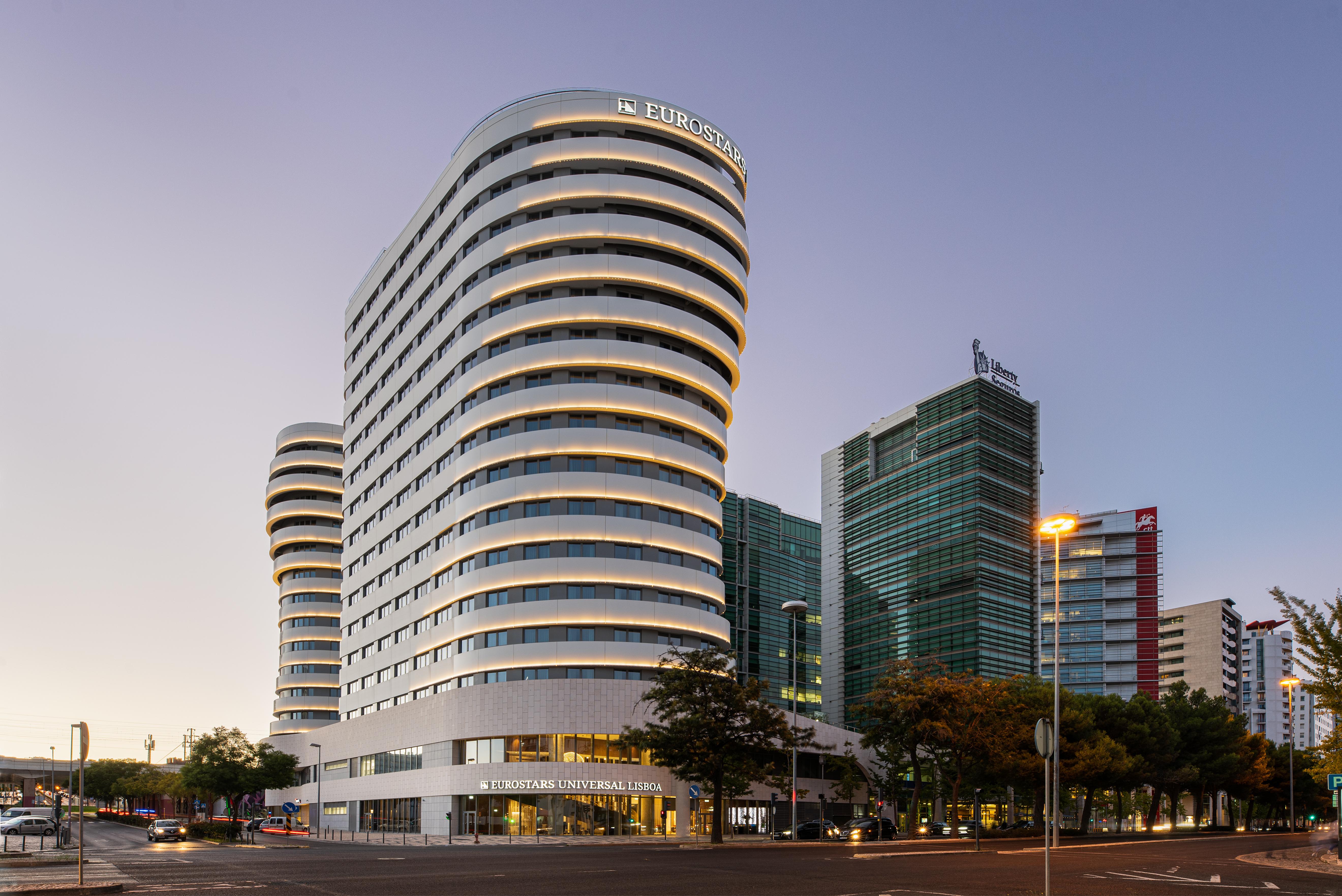 Отель Eurostars Universal Lisboa Экстерьер фото The photo features a modern architectural scene with two prominent buildings. The building on the left has a distinctive curved design with multiple horizontal lines, giving it a sleek and contemporary appearance. It appears to have multiple floors a