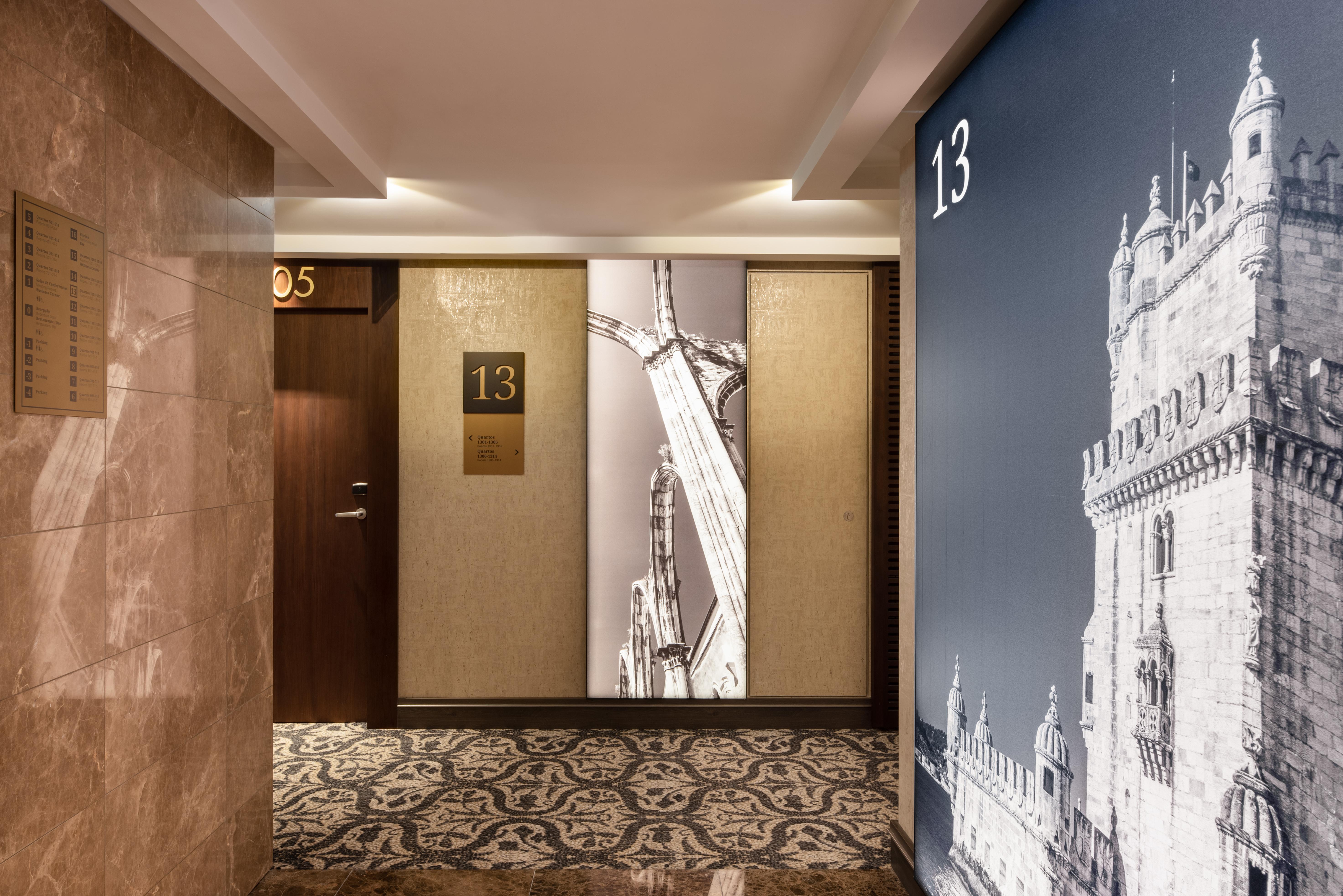 Отель Eurostars Universal Lisboa Экстерьер фото The photo shows a hotel corridor featuring room doors on one side. The door marked "13" is prominently displayed with a gold plaque. Adjacent to it, there is a decorative wall panel with an artistic representation of a landmark, possibly a building o