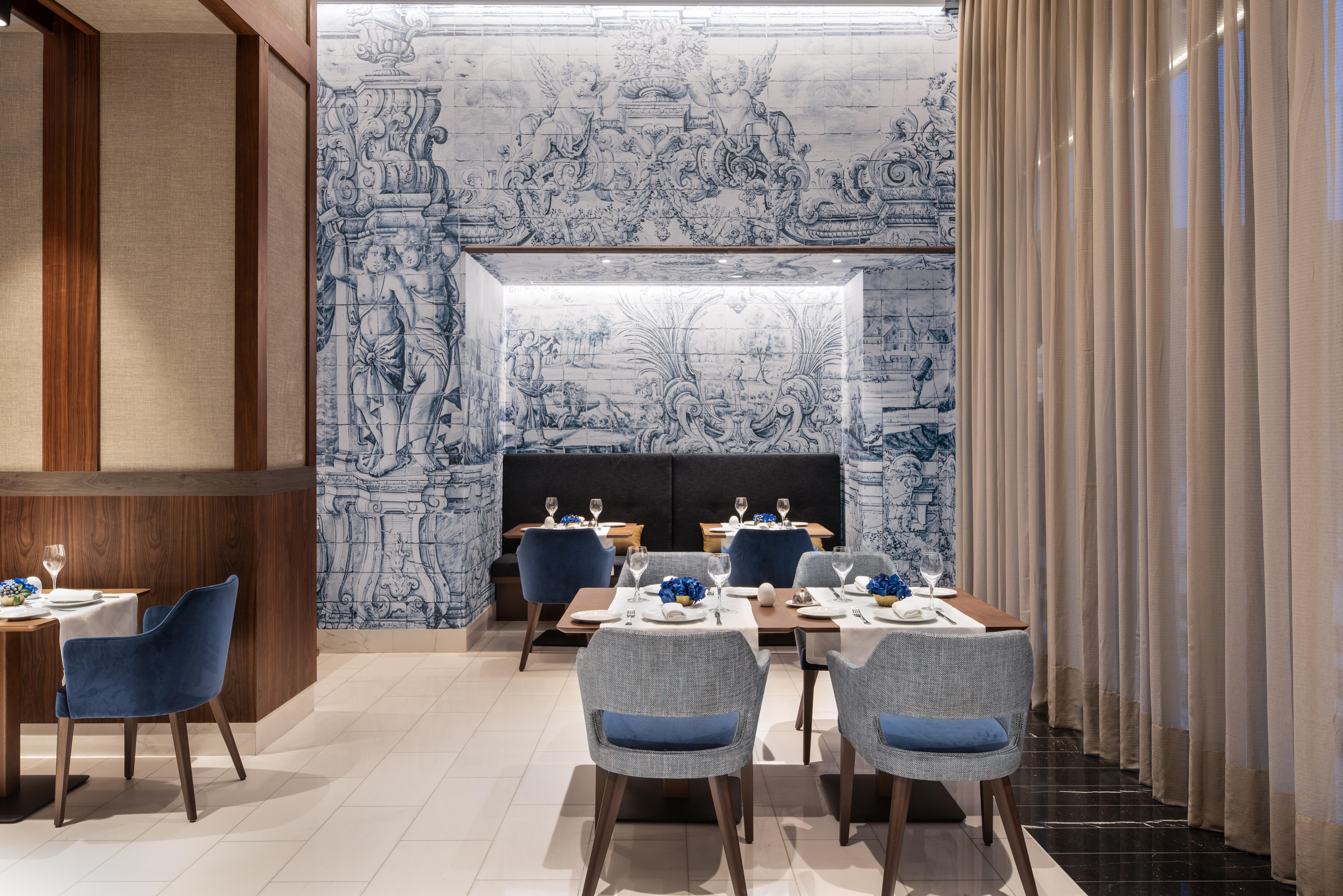 Отель Eurostars Universal Lisboa Экстерьер фото The photo depicts an elegant dining area in a restaurant. The interior features modern furnishings with blue upholstered chairs and wooden tables. A striking mural, likely inspired by classical art, serves as a backdrop on one wall, featuring intrica