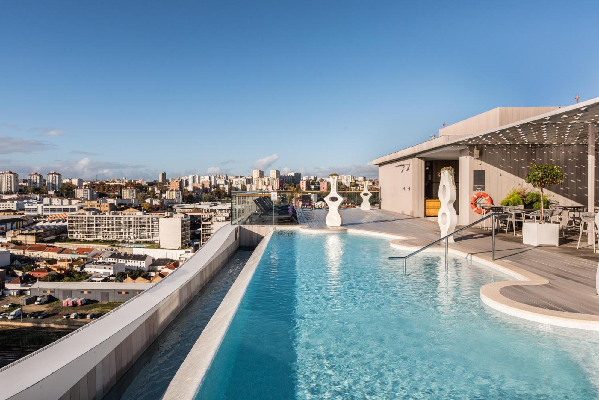 Отель Eurostars Universal Lisboa Экстерьер фото The photo features a luxurious rooftop infinity pool overlooking a city skyline. The pool has a sleek design, with clean lines and a smooth surface that reflects the sky. Surrounding the pool area, there are modern loungers and stylish decor. In the 